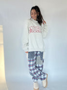 Woman wearing a light gray sweatshirt with 'MERRY' and plaid pants against a white background