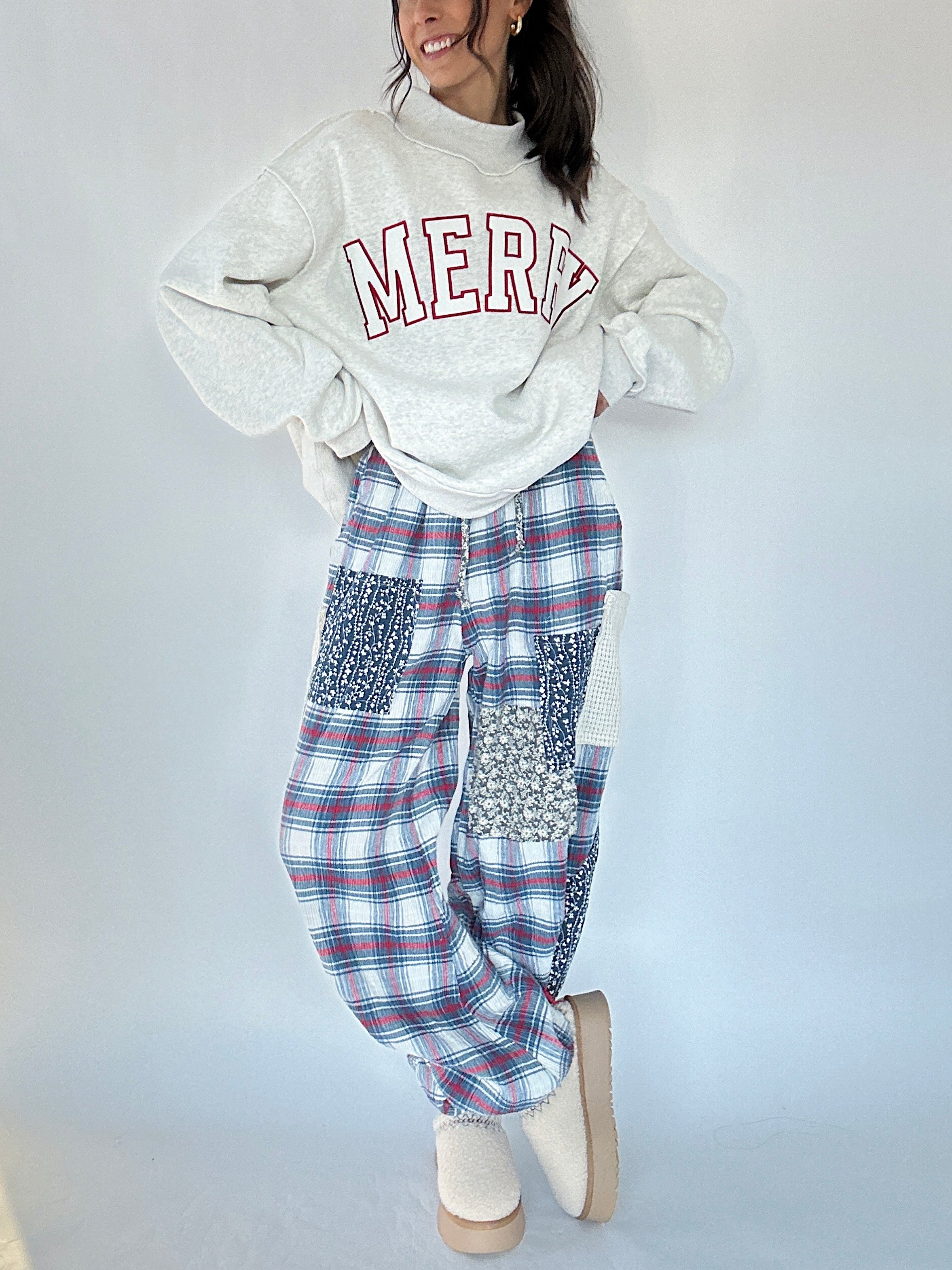 Person wearing a white sweatshirt with 'MERRY' text and plaid pants on a plain background
