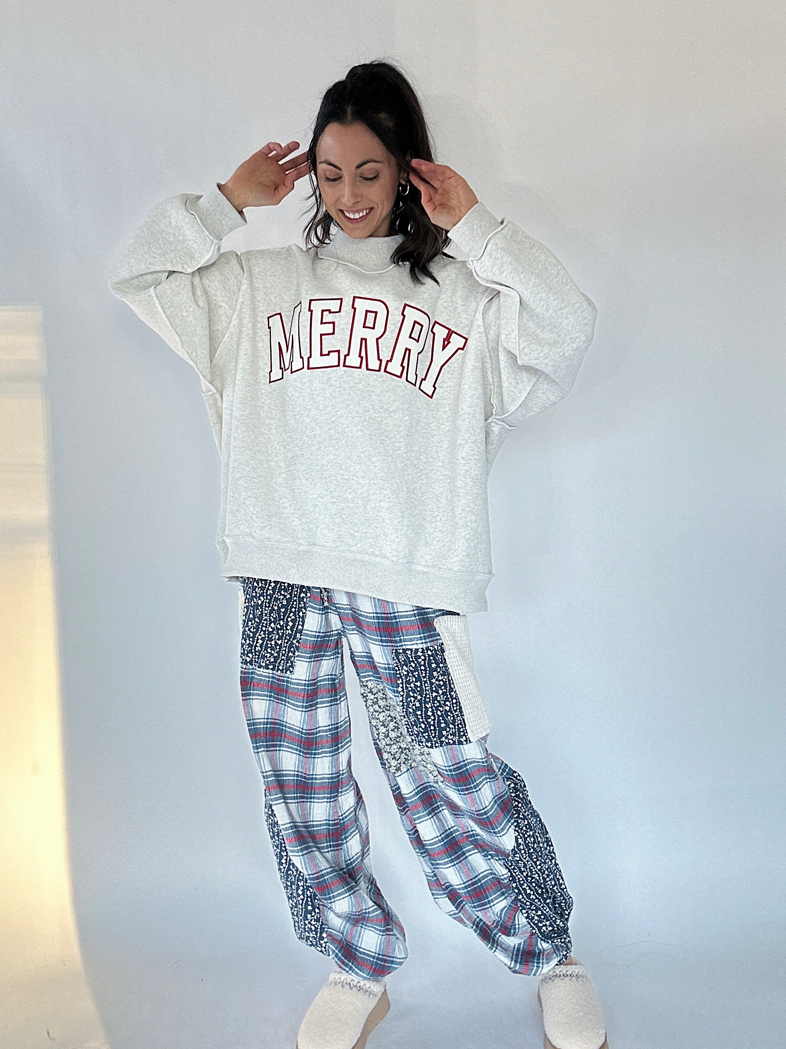 Person wearing a 'MERRY' sweatshirt and plaid pants against a plain background