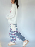 Person wearing a grey sweatshirt with text and plaid pants on a plain background