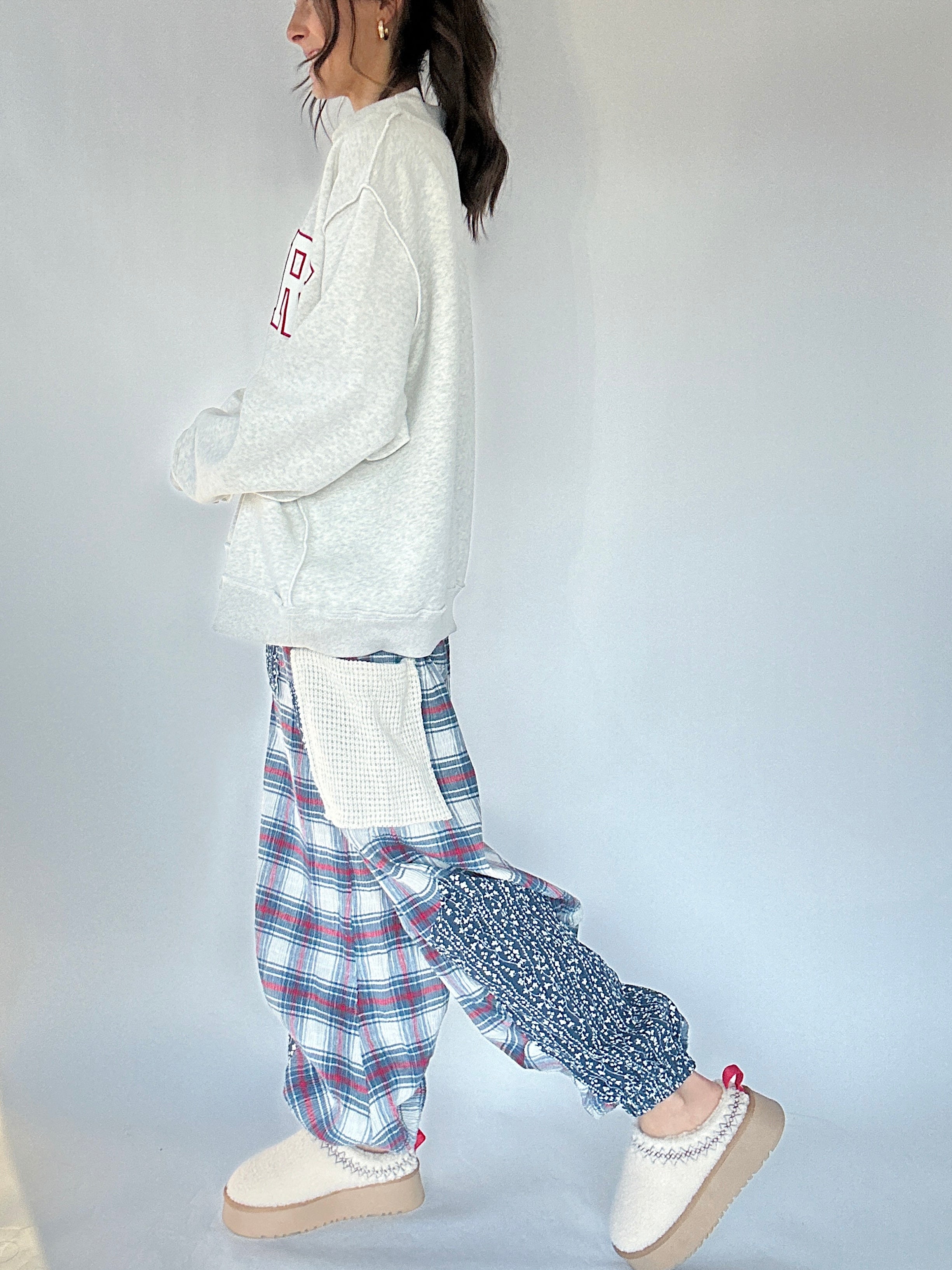 Person wearing a grey sweatshirt with text and plaid pants on a plain background