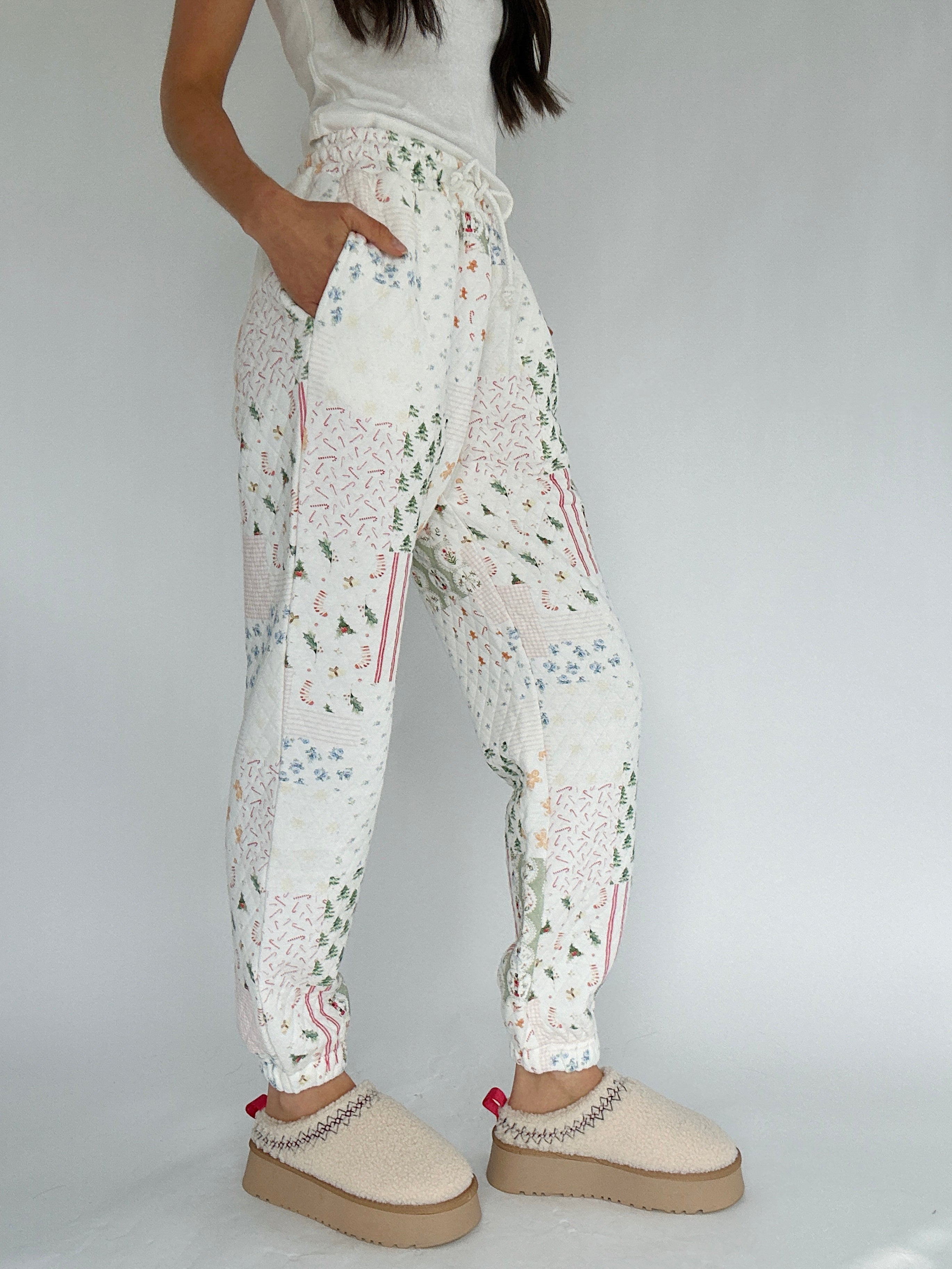 Person wearing white quilted holiday-patterned jogger pants with beige clogs on a plain background