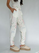 Person wearing white quilted holiday-patterned jogger pants with beige clogs on a plain background