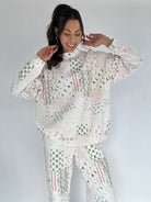 Woman wearing a white quilted mock neck with mixed holiday patterns and matching pants against a plain background