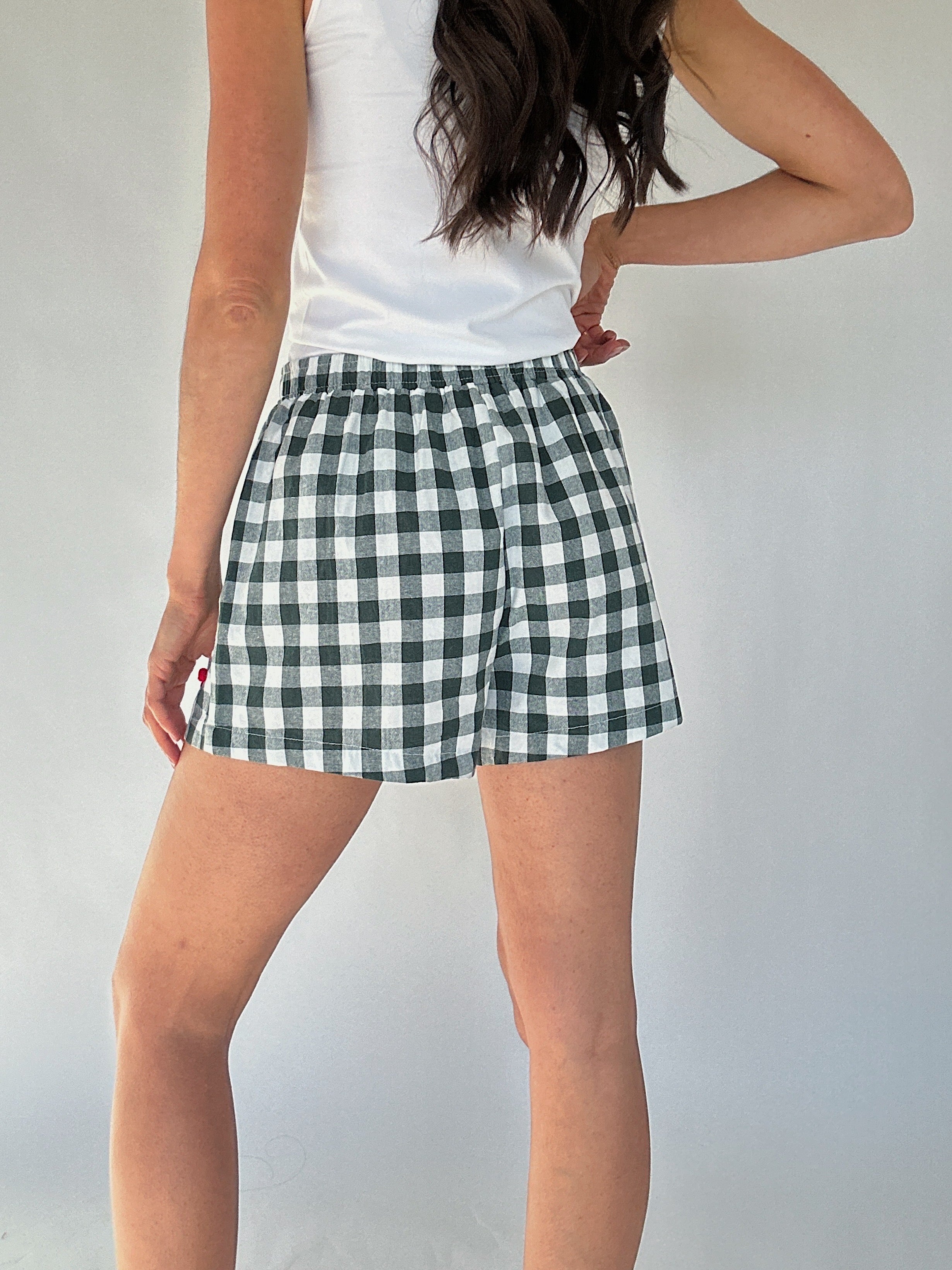 Person wearing green and white checkered shorts on a plain background to show back view