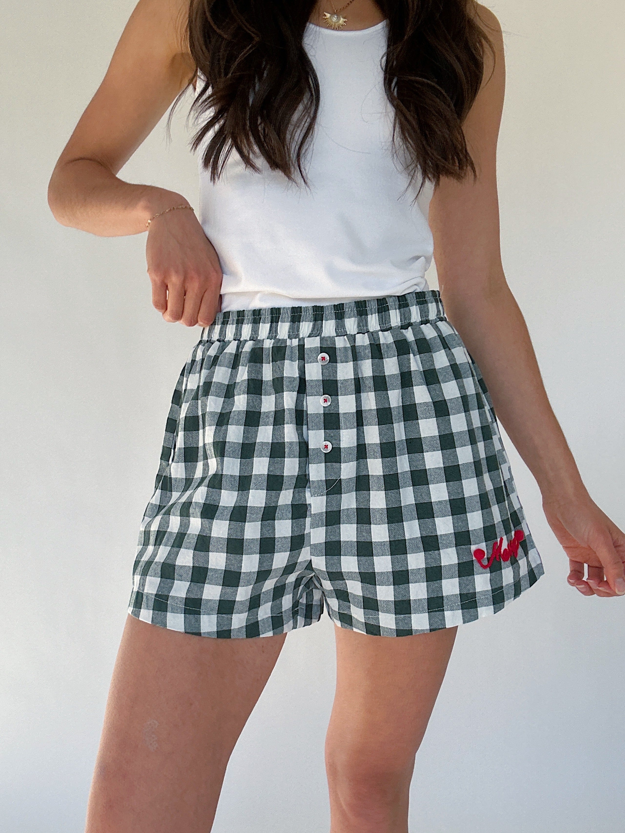 Person wearing green and white checkered shorts with red "merry" and elastic waistband on a plain background
