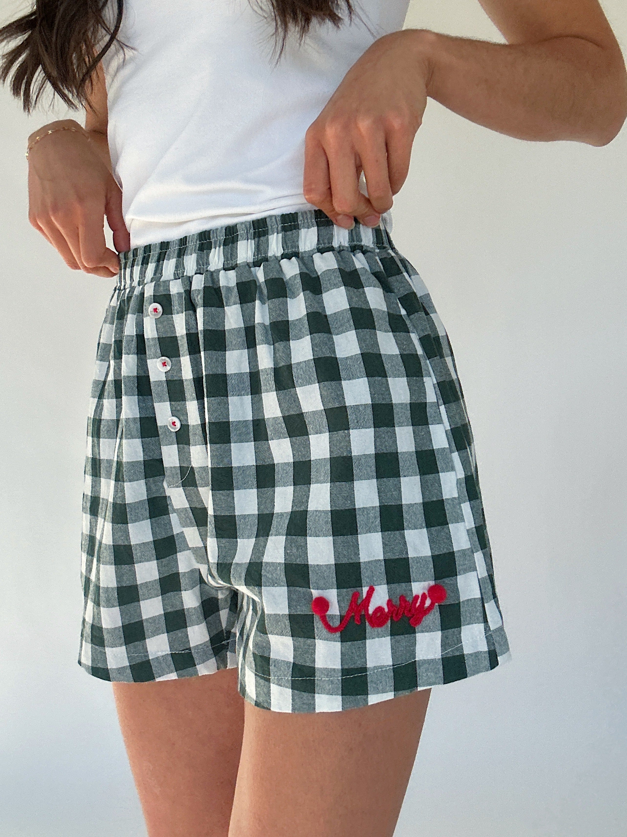 Green and white checkered boxer shorts with red "merry" lettering worn by a person on a plain background