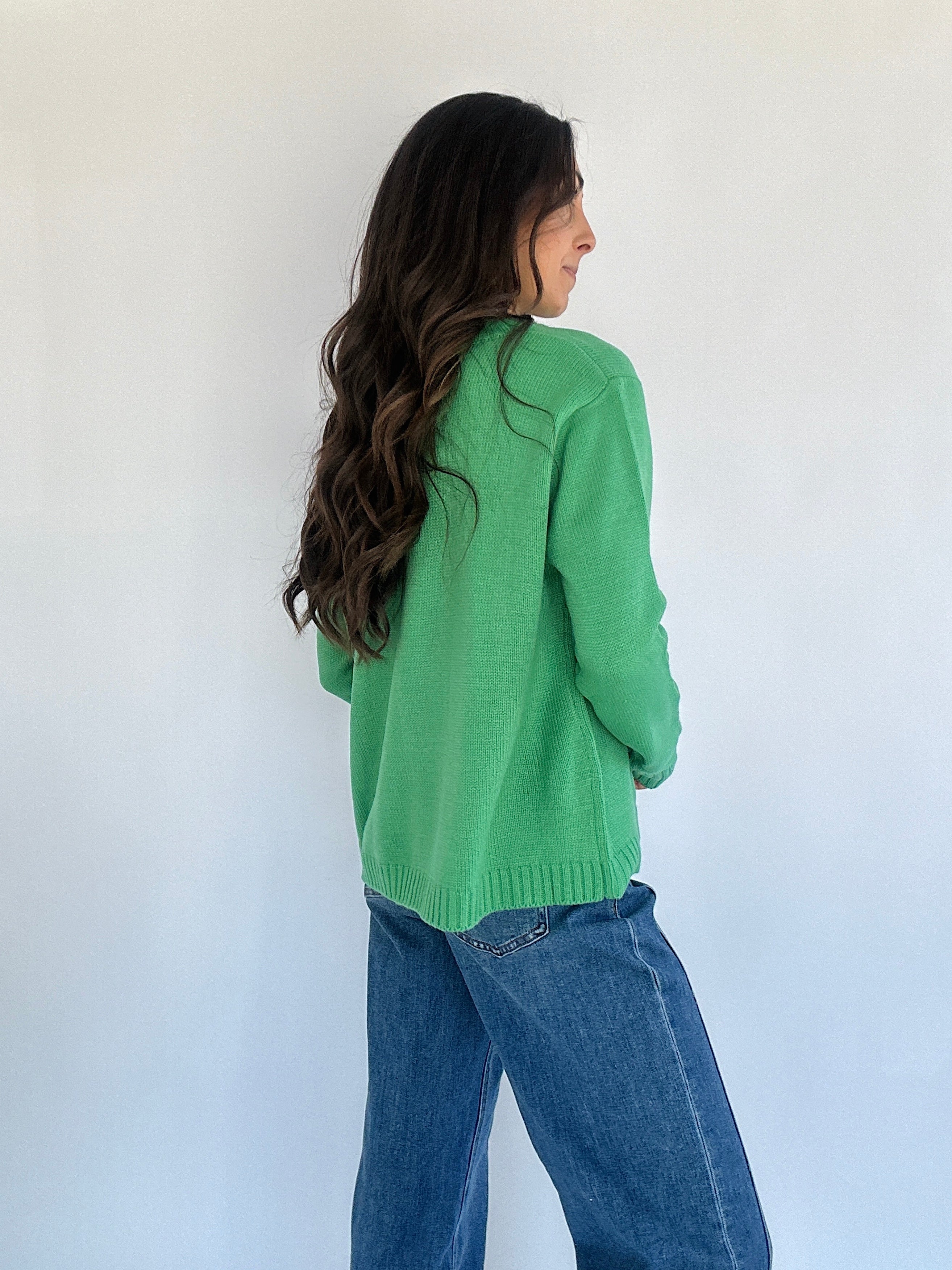 Woman wearing green sweater and blue jeans on a plain background from back