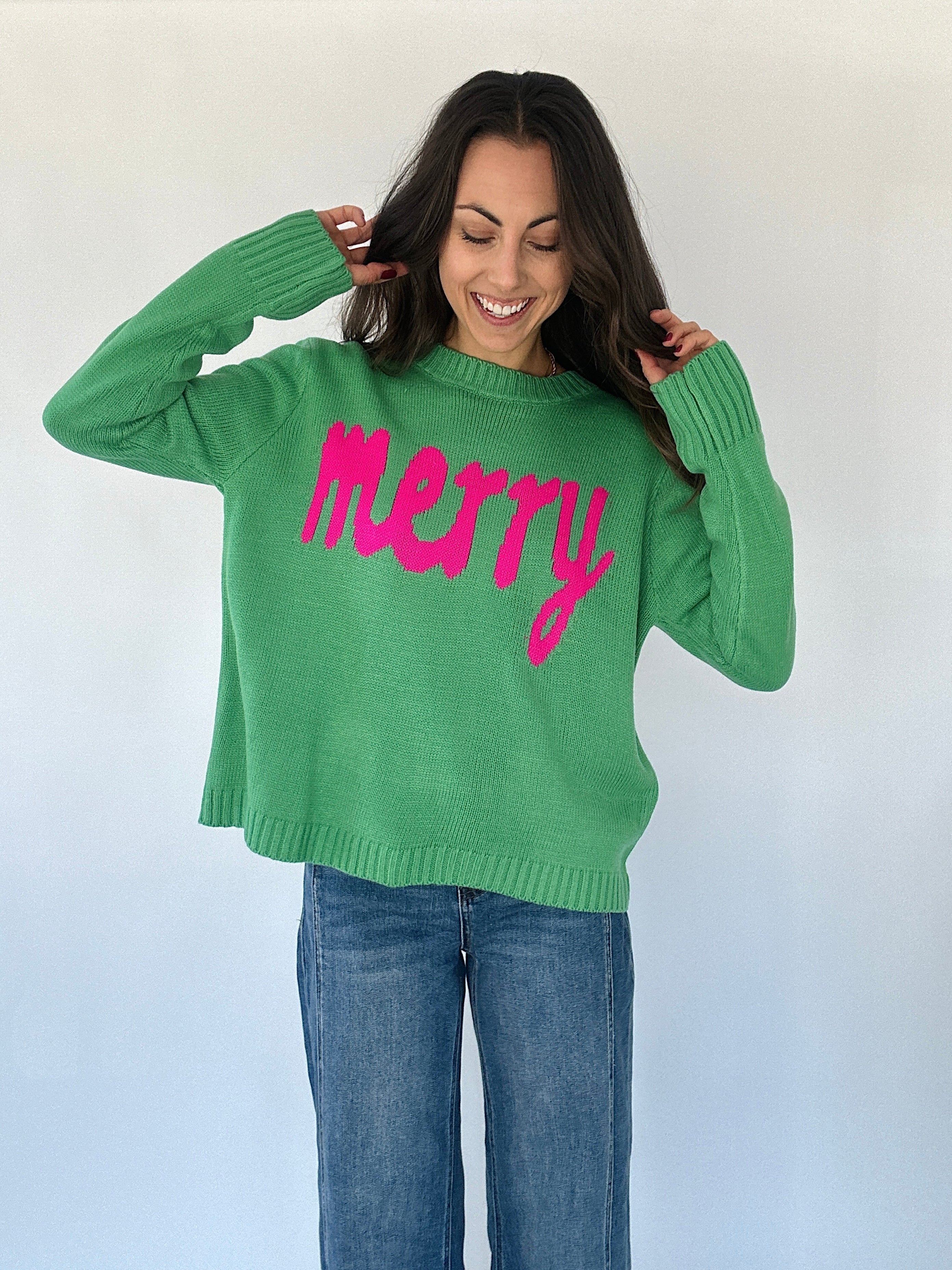 Woman wearing a green sweater with pink ' merry ' lettering
