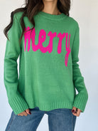Green sweater with pink 'merry' lettering and blue jeans