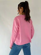 Person wearing a pink sweater and blue jeans against a white background from back