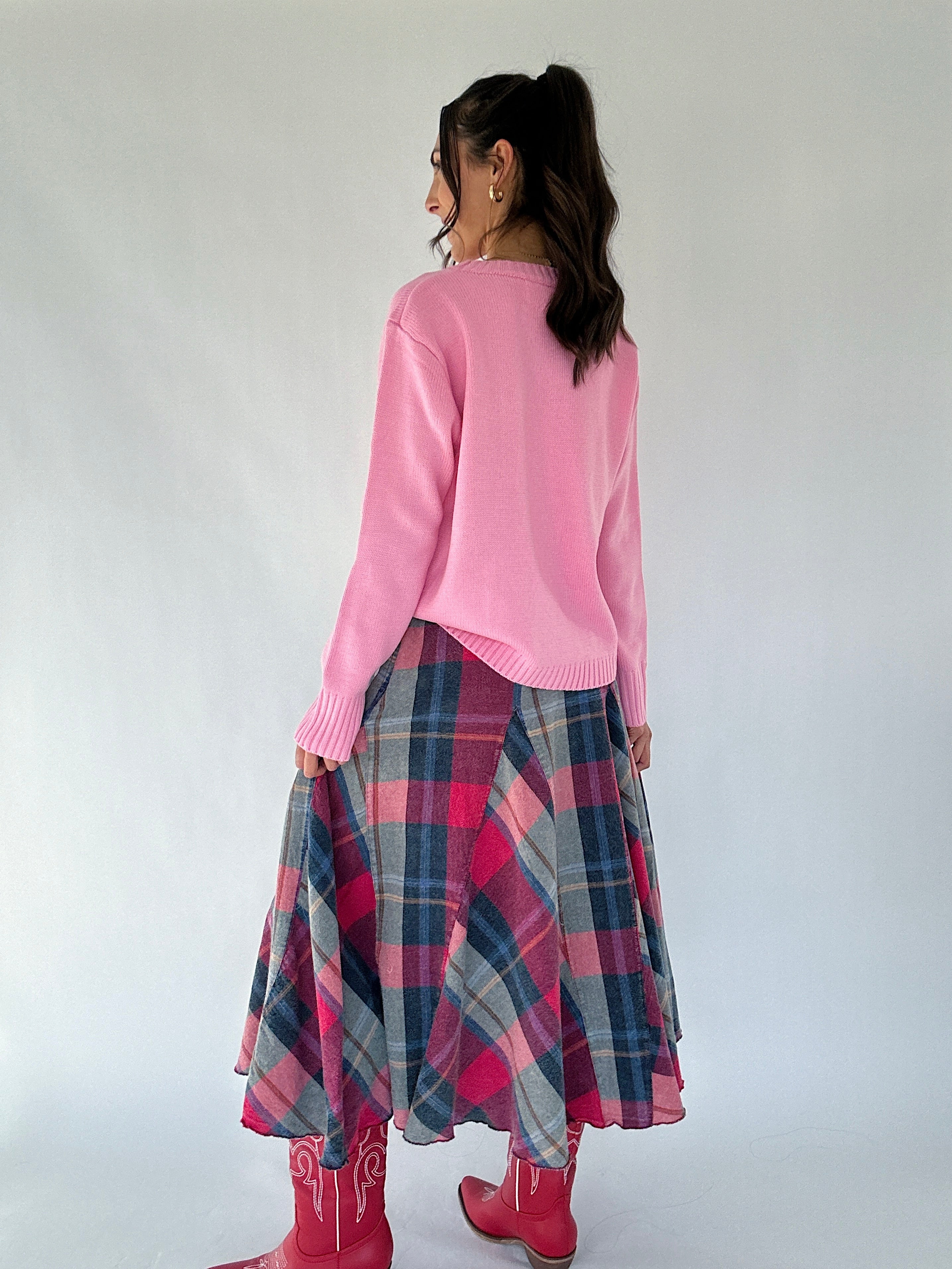 Person wearing a pink sweater and plaid skirt with red boots on a white background from back