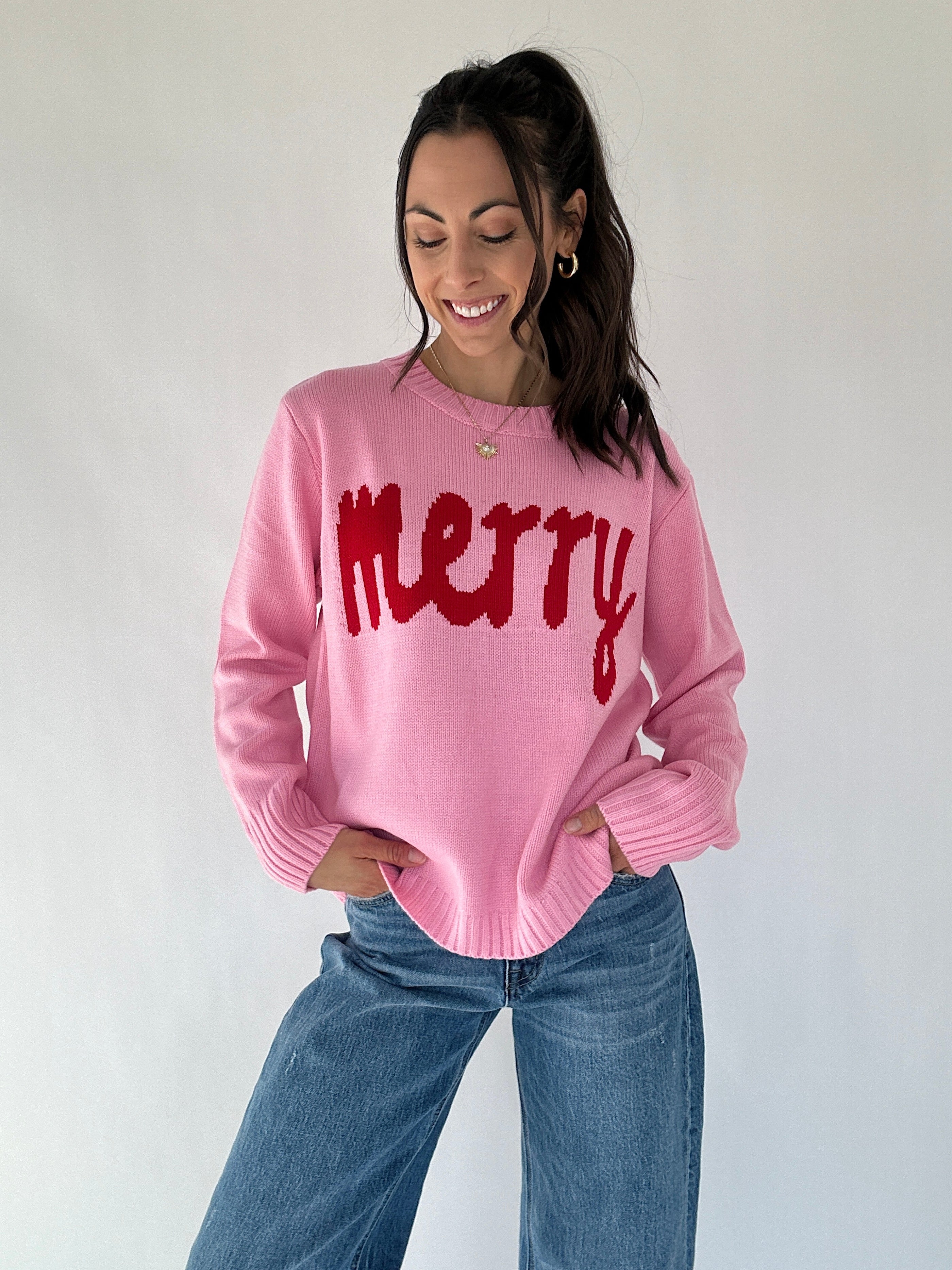 Woman wearing a pink sweater with 'merry' text against a plain background