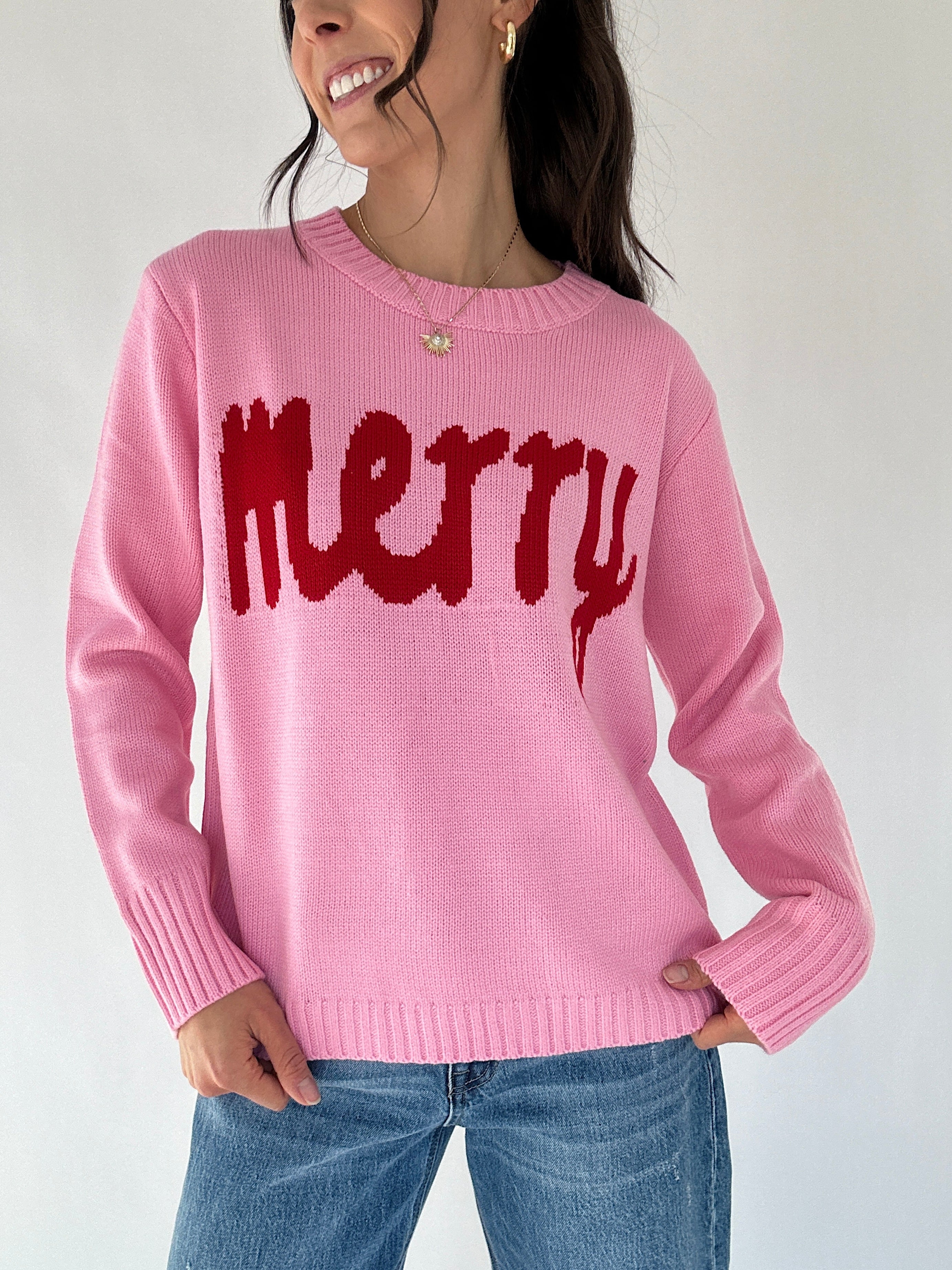 Person wearing a pink sweater with red 'merry' text on a plain background