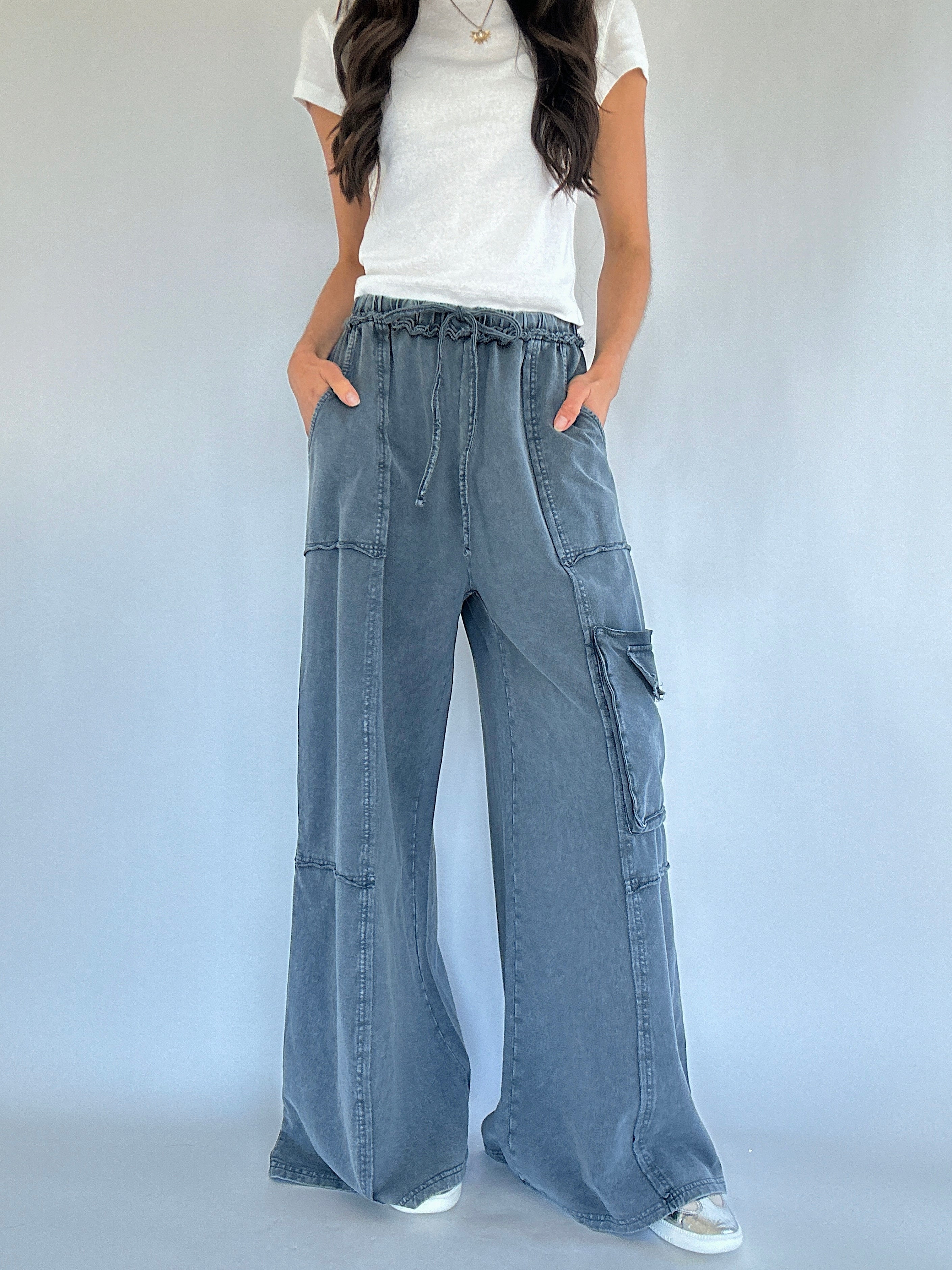Person wearing smoke blue cargo pants and a white top on a plain background