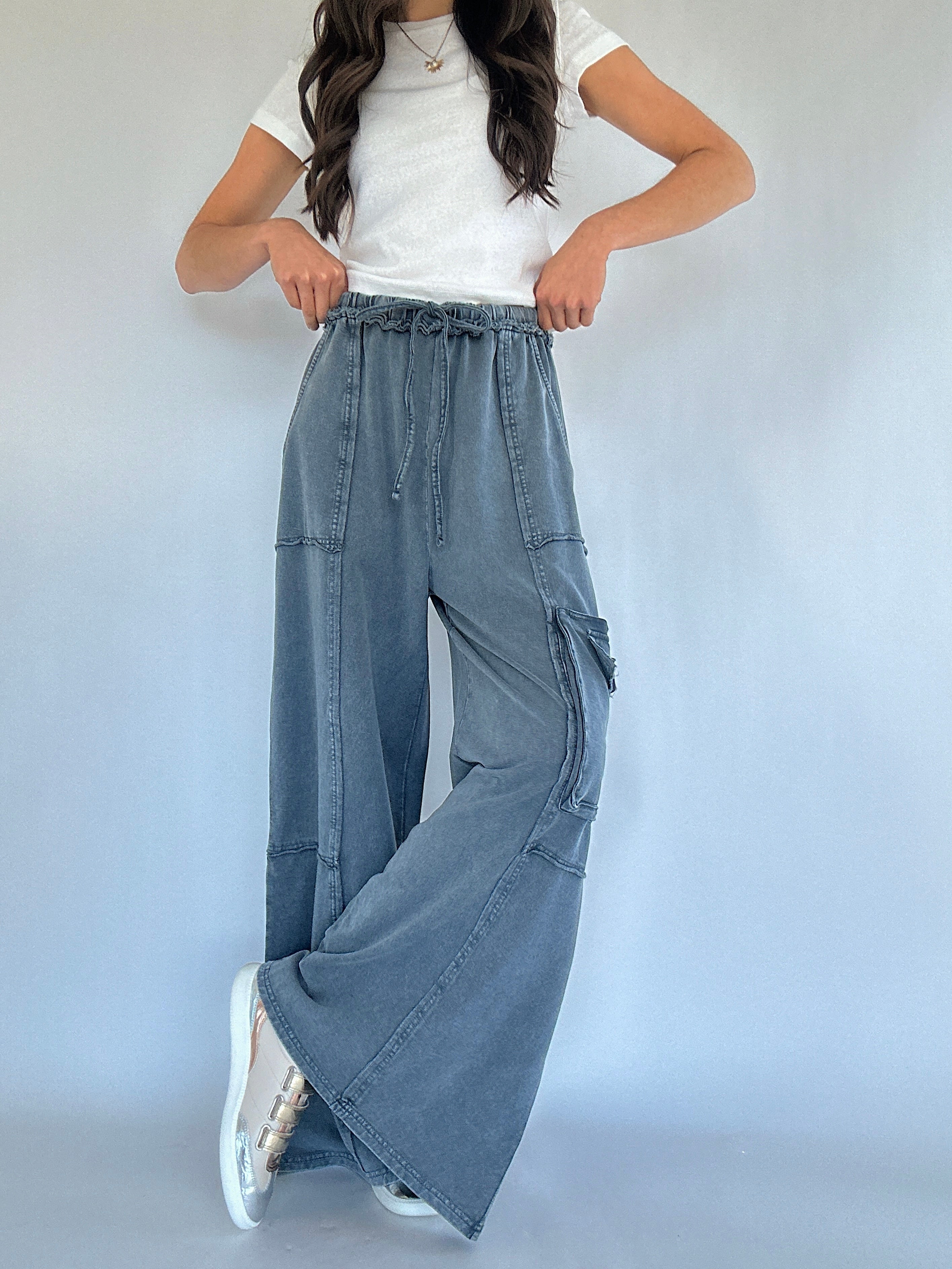 Person wearing smoke blue cargo pants and a white top on a plain background