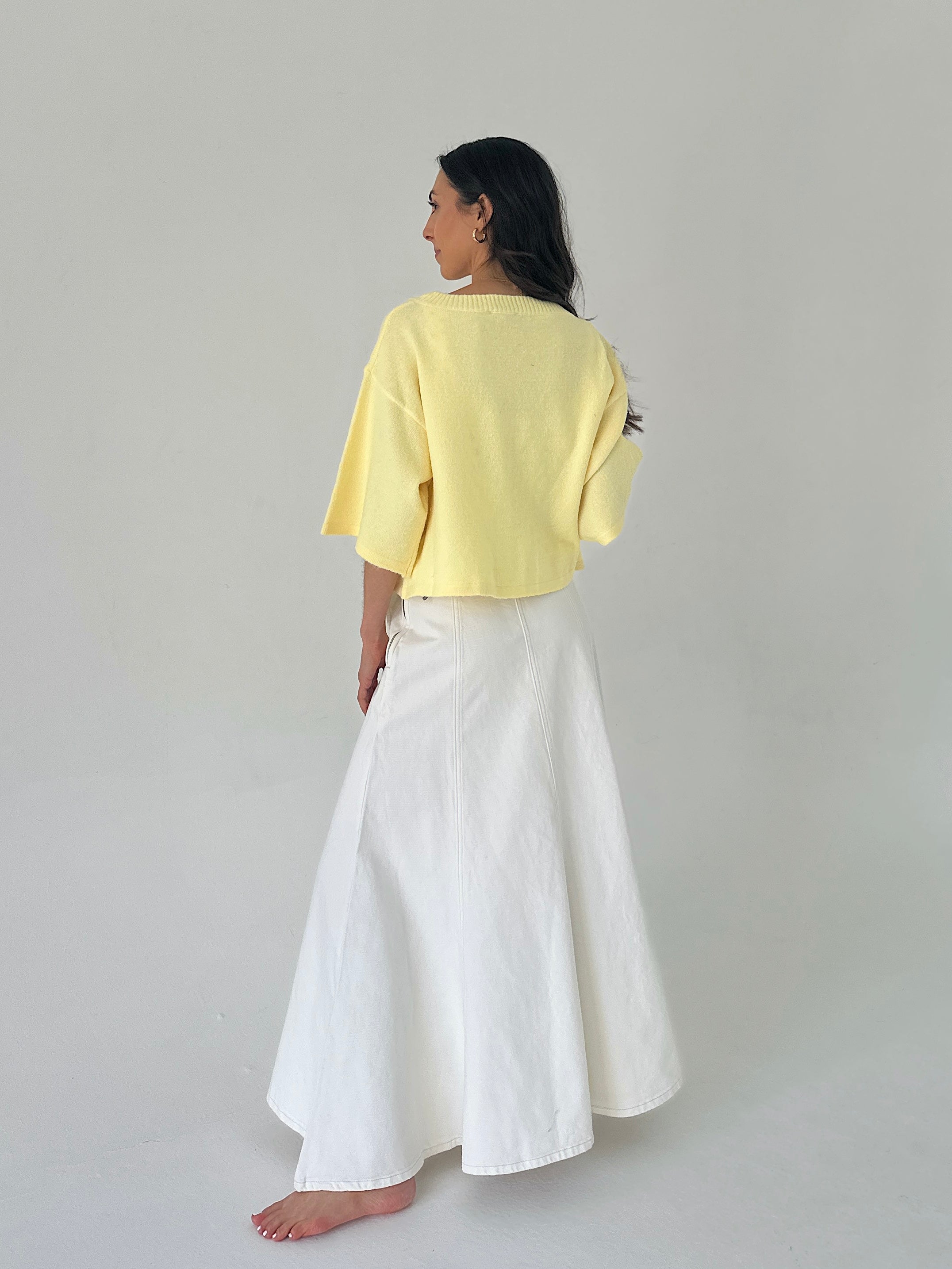 Woman wearing a yellow top and white pants on a plain background