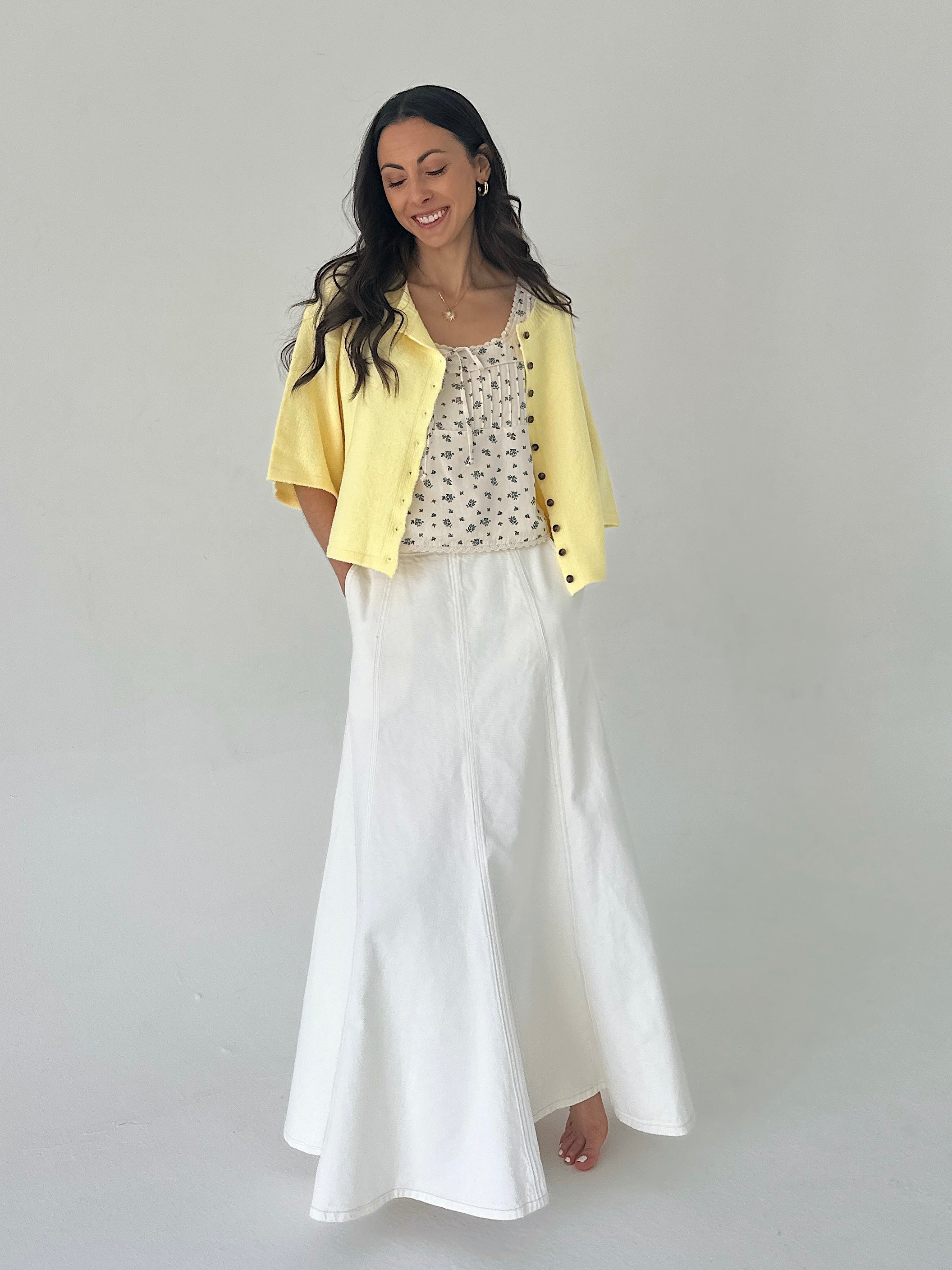 Woman wearing a yellow cardigan, patterned top, and white pants on a plain background