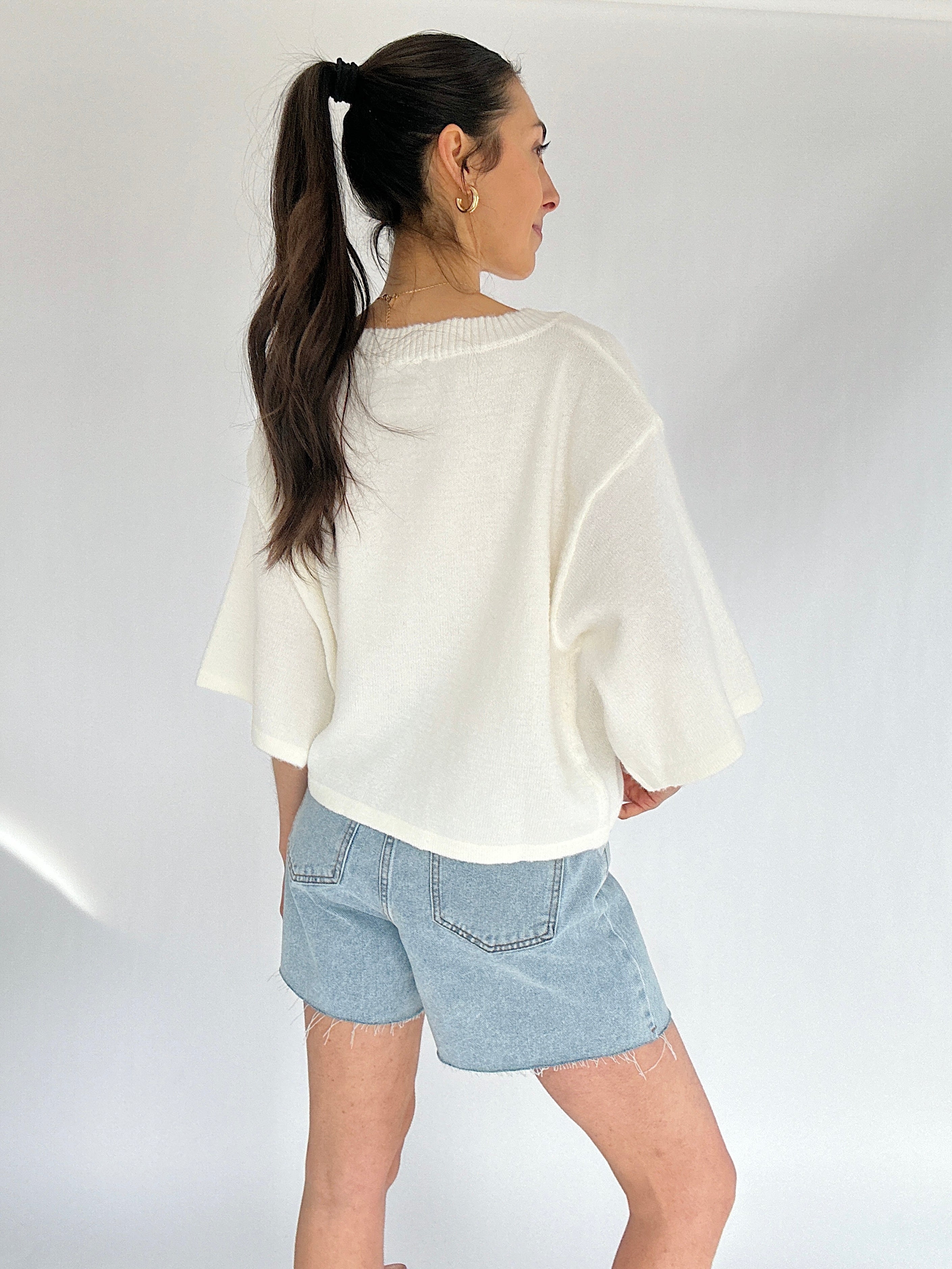 Woman wearing a white sweater and light blue denim shorts on a plain background
