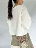 Woman wearing a white sweater over a patterned skirt on a plain background from back
