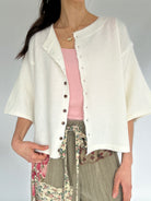 Person wearing a white cardigan over a pink top and floral pants on a gray background