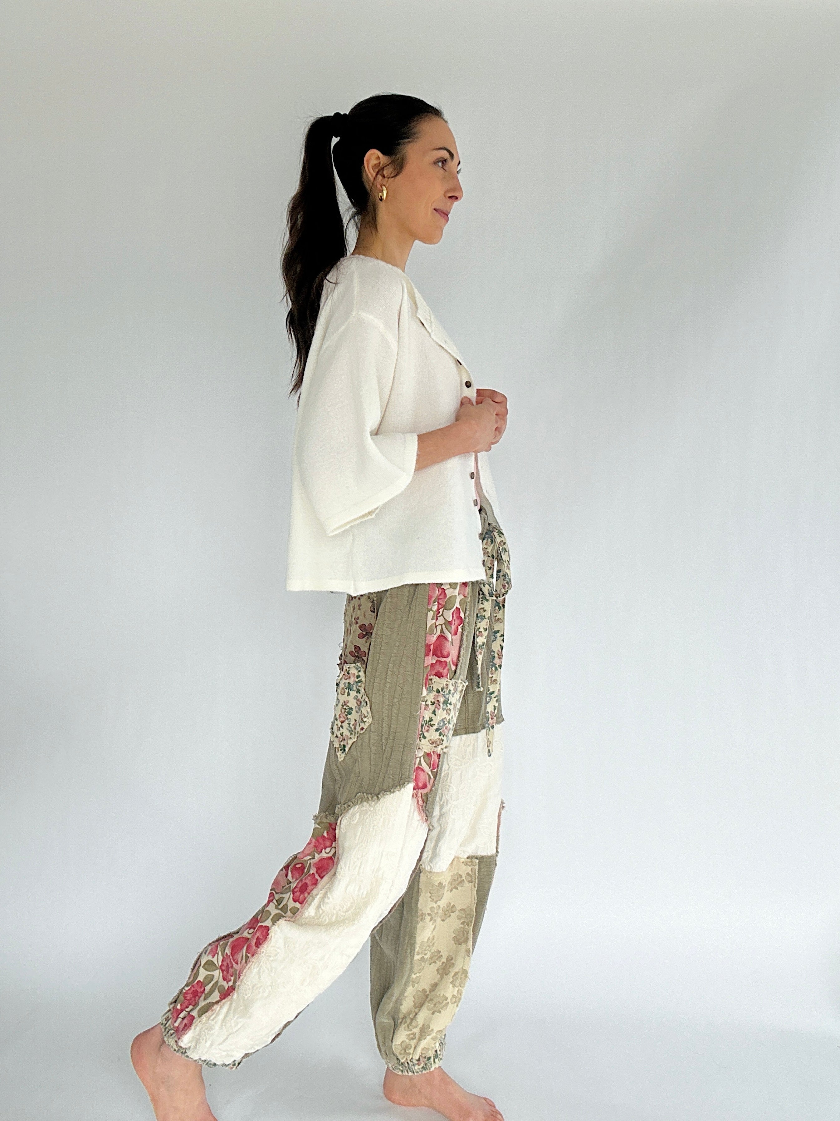 Woman wearing a white top and floral pants against a plain background from side