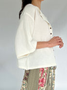 Person wearing a white cardigan with floral pants on a plain background from side