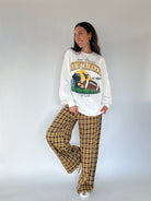 Woman wearing a 'West Virginia Mountaineers' sweatshirt and plaid pants against a white background