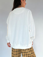 Person wearing a white oversized sweatshirt and plaid pants on a plain background showing the back