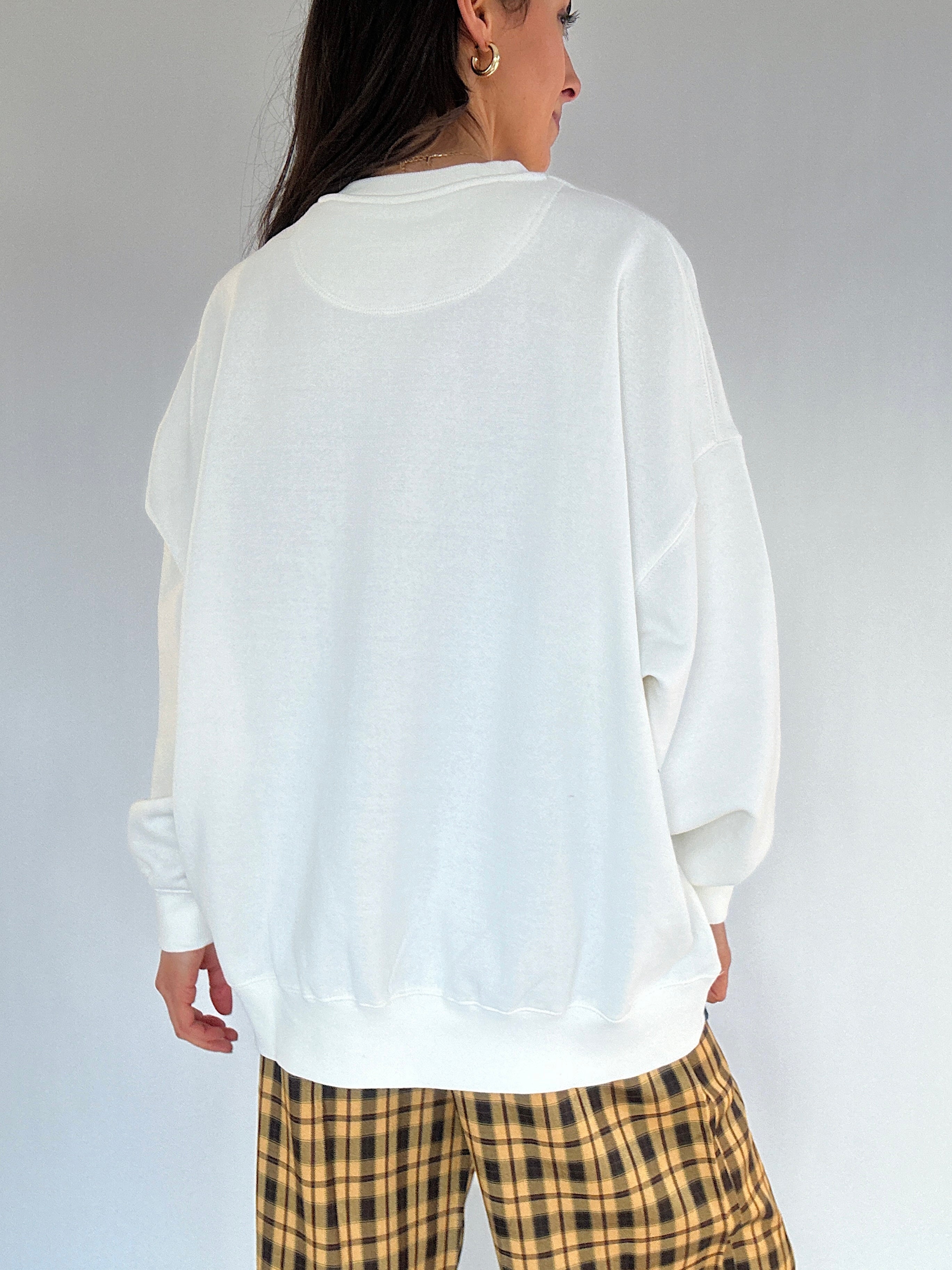 Person wearing a white oversized sweatshirt and plaid pants on a plain background showing the back