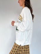 Woman wearing a white long-sleeve sweatshirt with text and plaid pants against a plain background showing the side