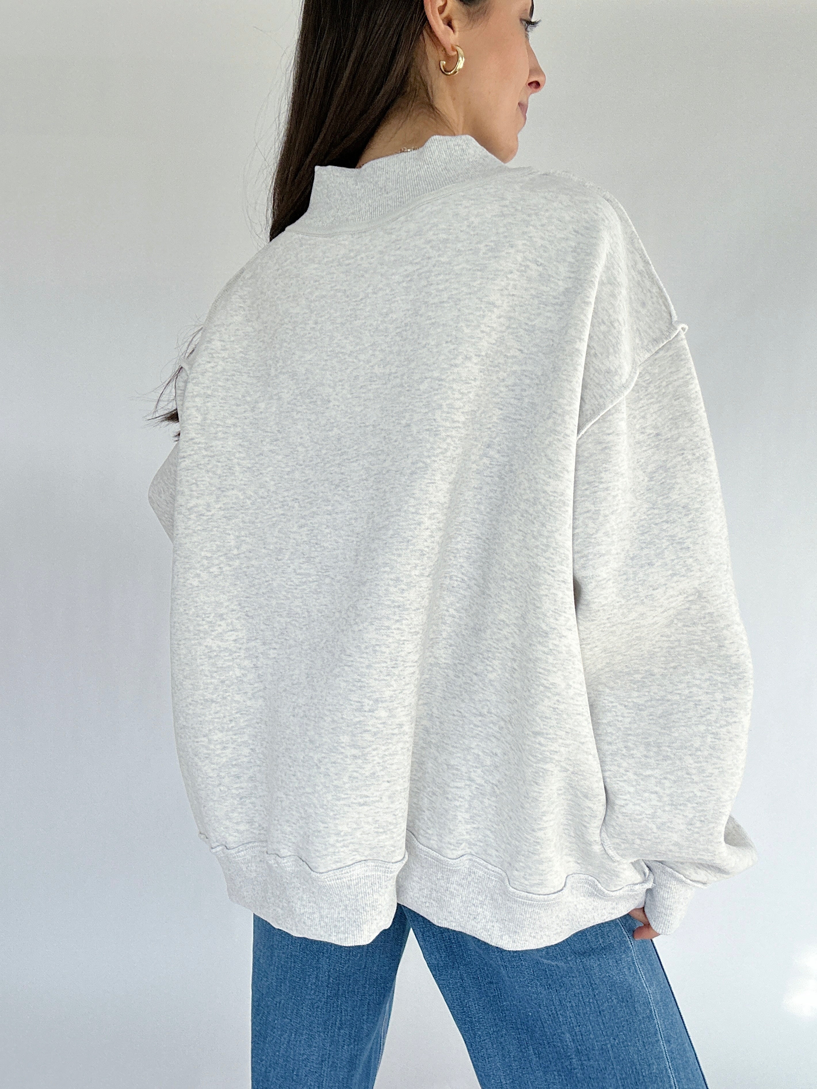 Person wearing a light gray sweatshirt and blue jeans on a white background showing back