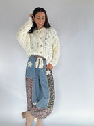 Woman wearing a cream textured cardigan and denim and leopard jogger pants on a plain background