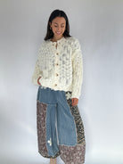 Woman wearing a cream knitted cardigan denim and leopard patterned jogger pants on a plain background