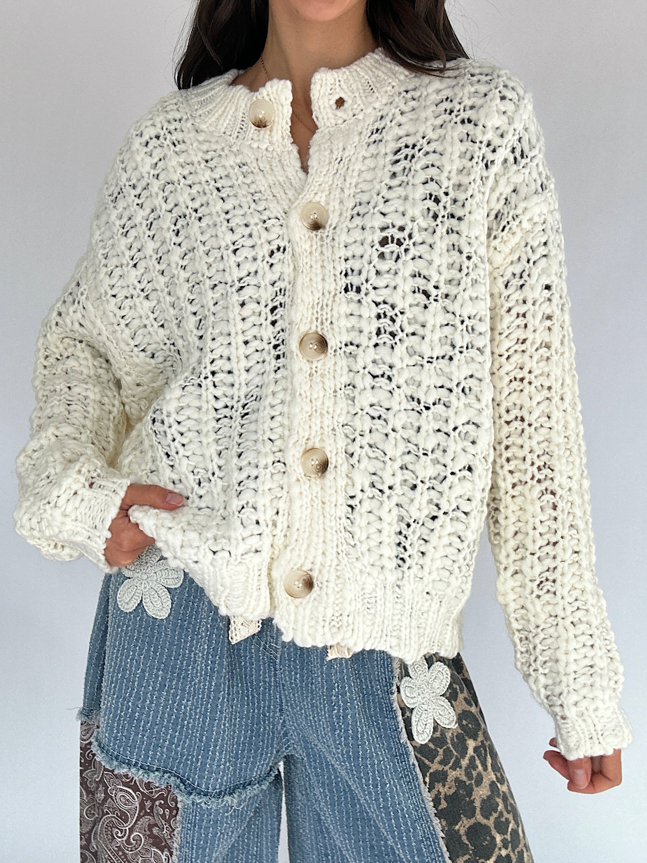 Person wearing a cream knitted button up cardigan with a plain background