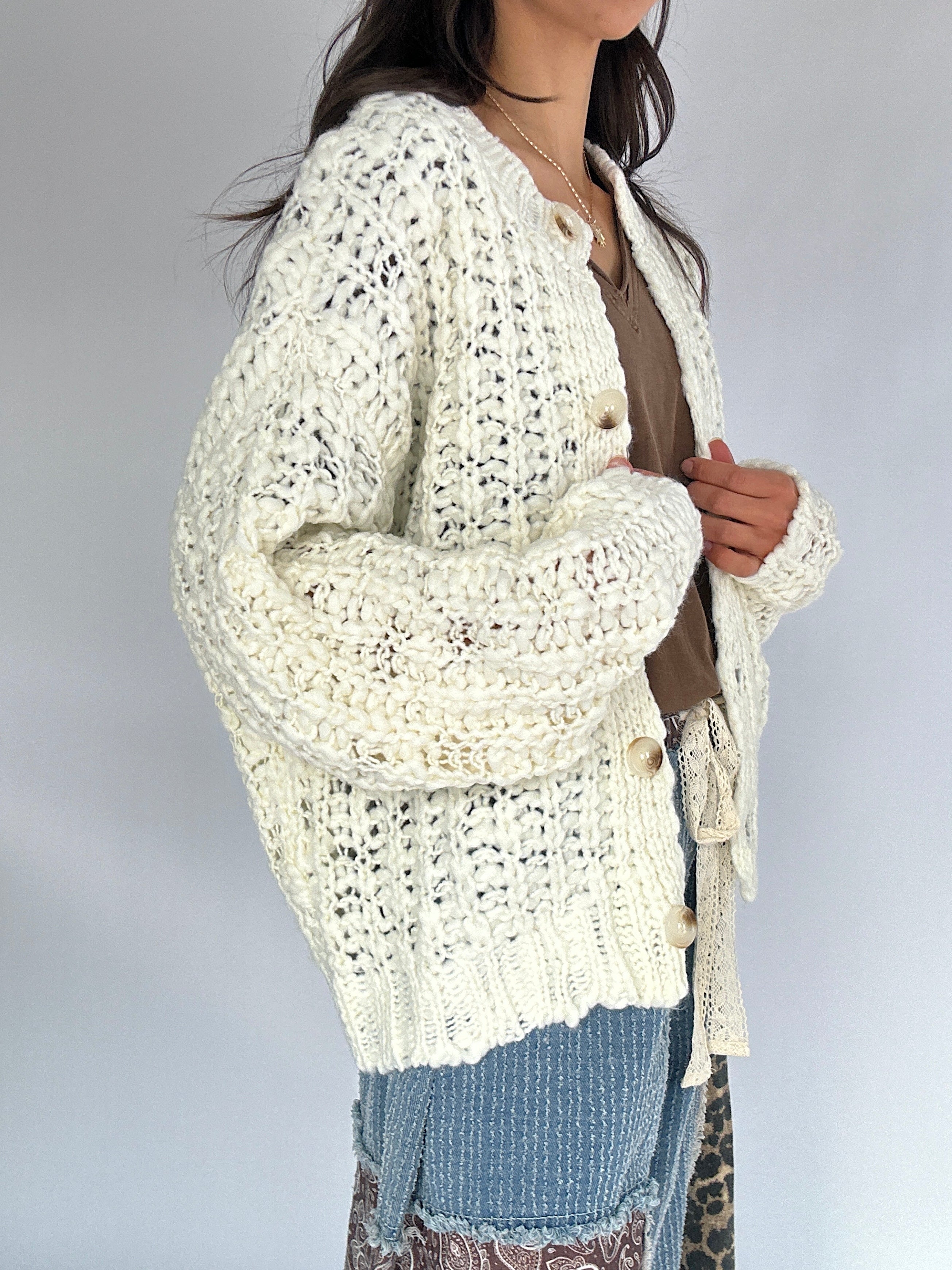 Person wearing a cream-colored crochet cardigan on a plain background from side