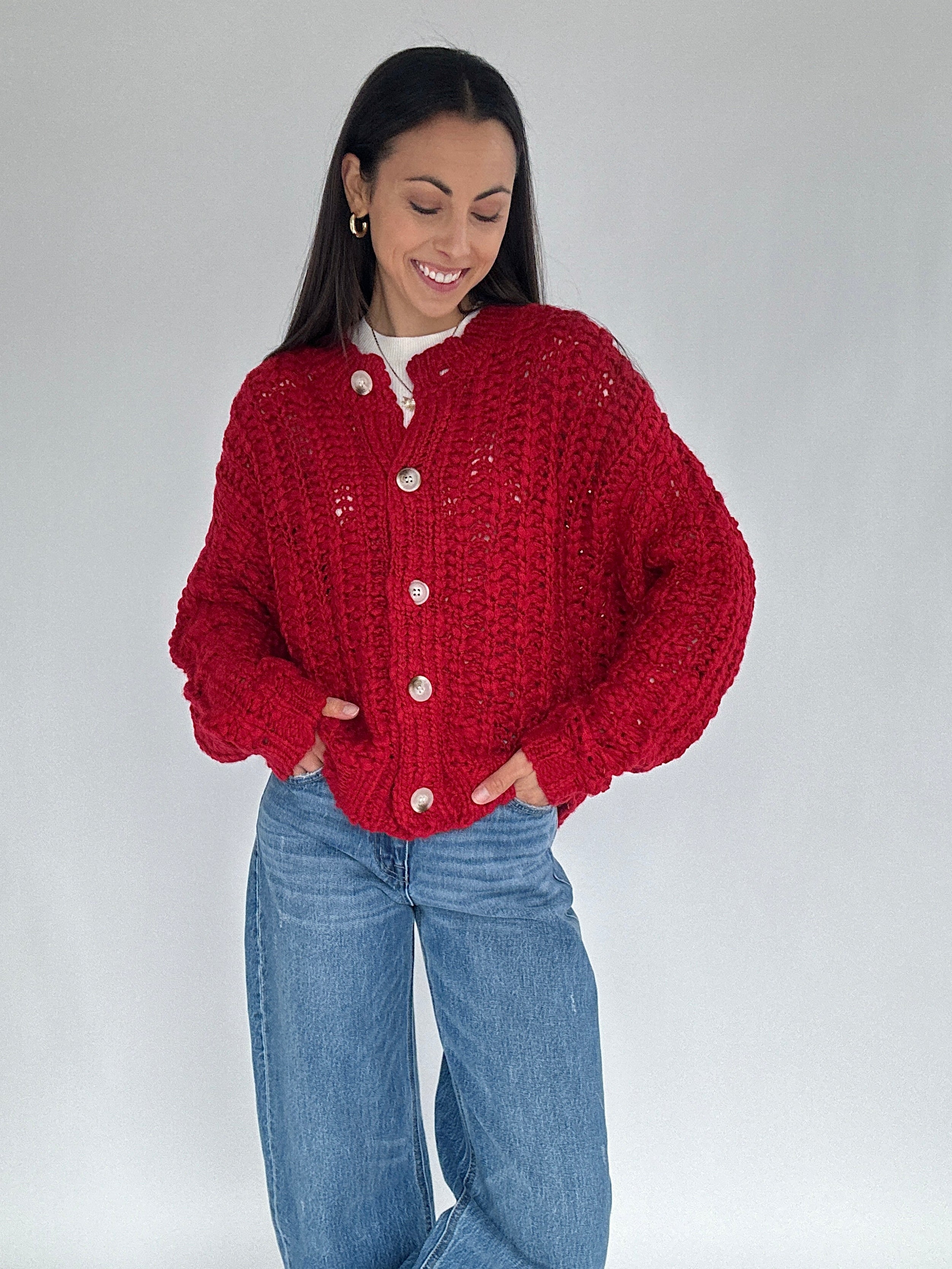 Woman wearing a red knitted cardigan and blue jeans on a white background