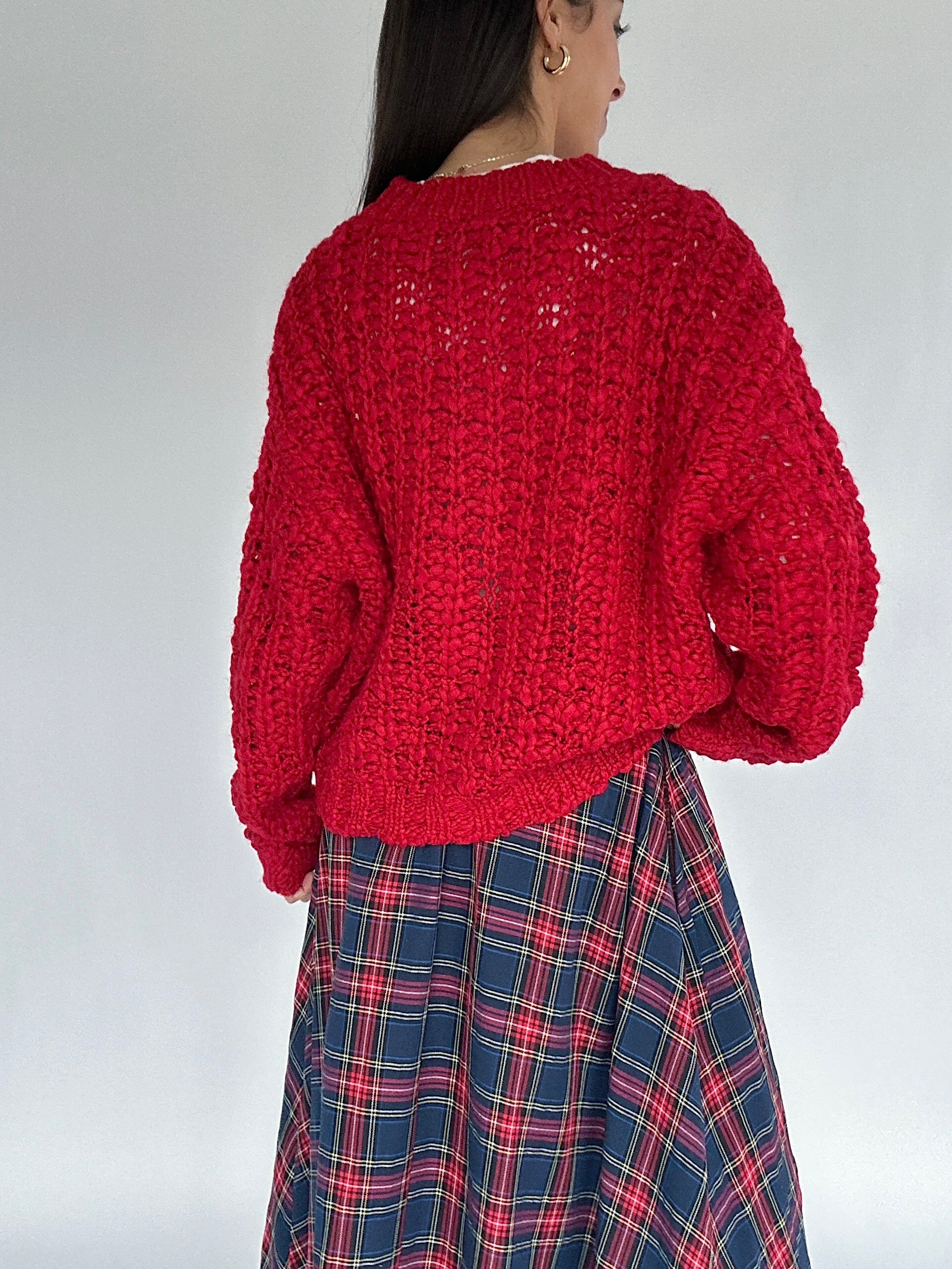 Person wearing a red knitted sweater and plaid skirt on a plain background back view