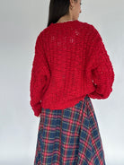 Person wearing a red knitted sweater and plaid skirt on a plain background back view