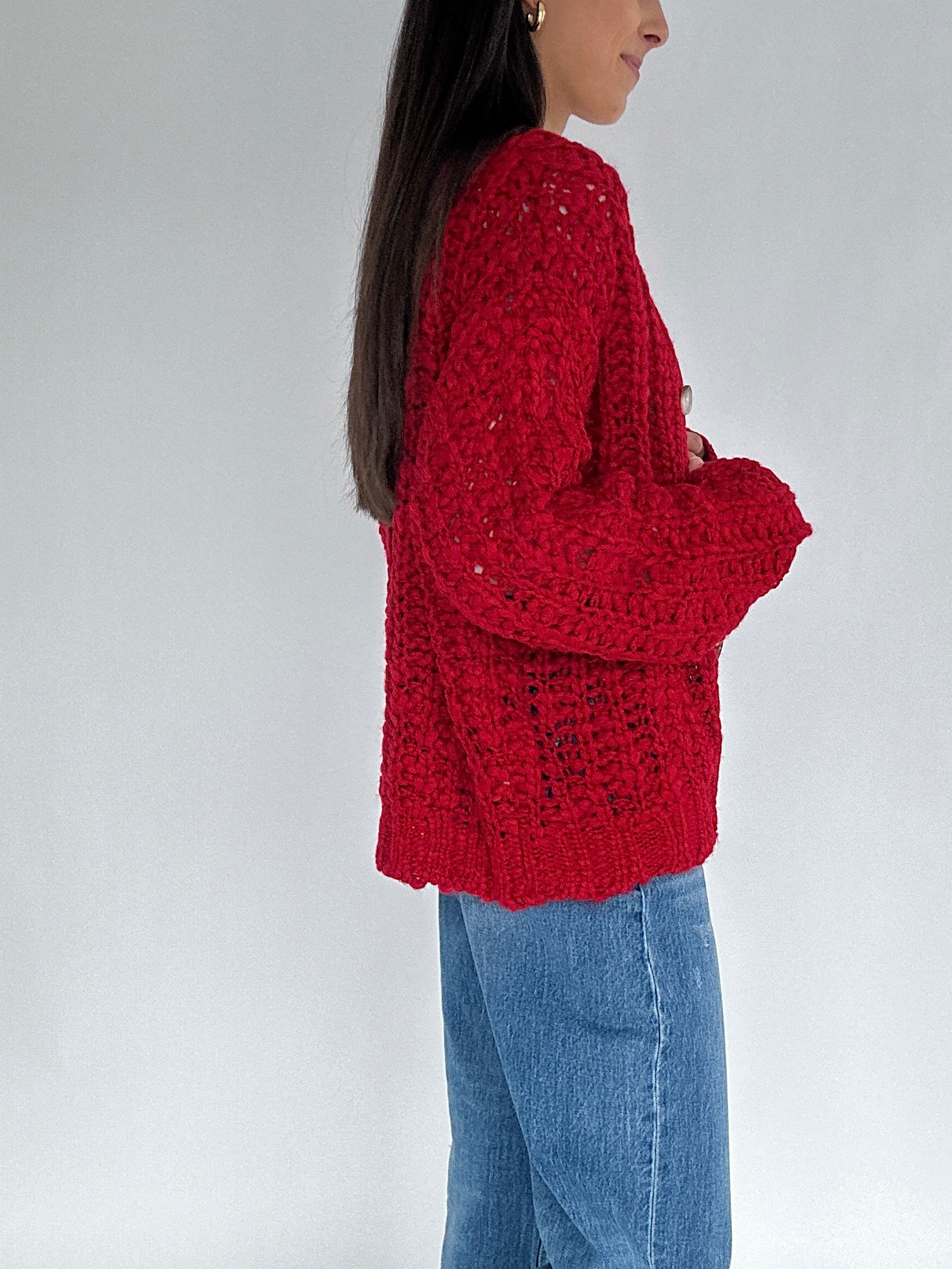 Person wearing a red knitted sweater and blue jeans on a plain background side view