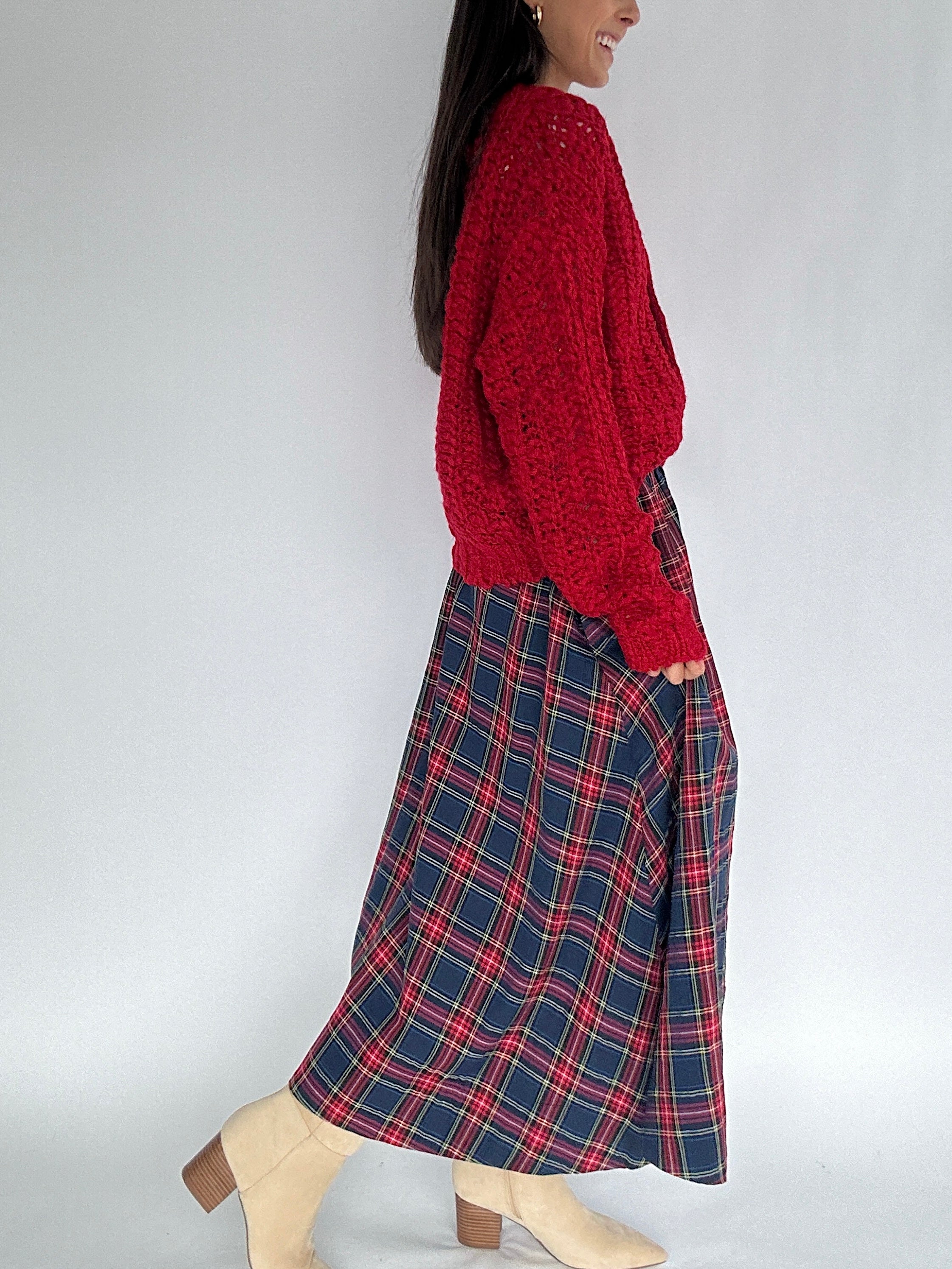 Person wearing a red sweater and plaid skirt on a white background from side