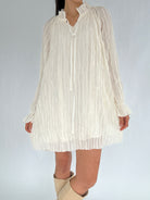 White pleated dress worn by a person on a plain background