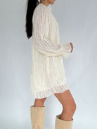 Person wearing a white long-sleeve dress with beige knee-high boots on a plain background