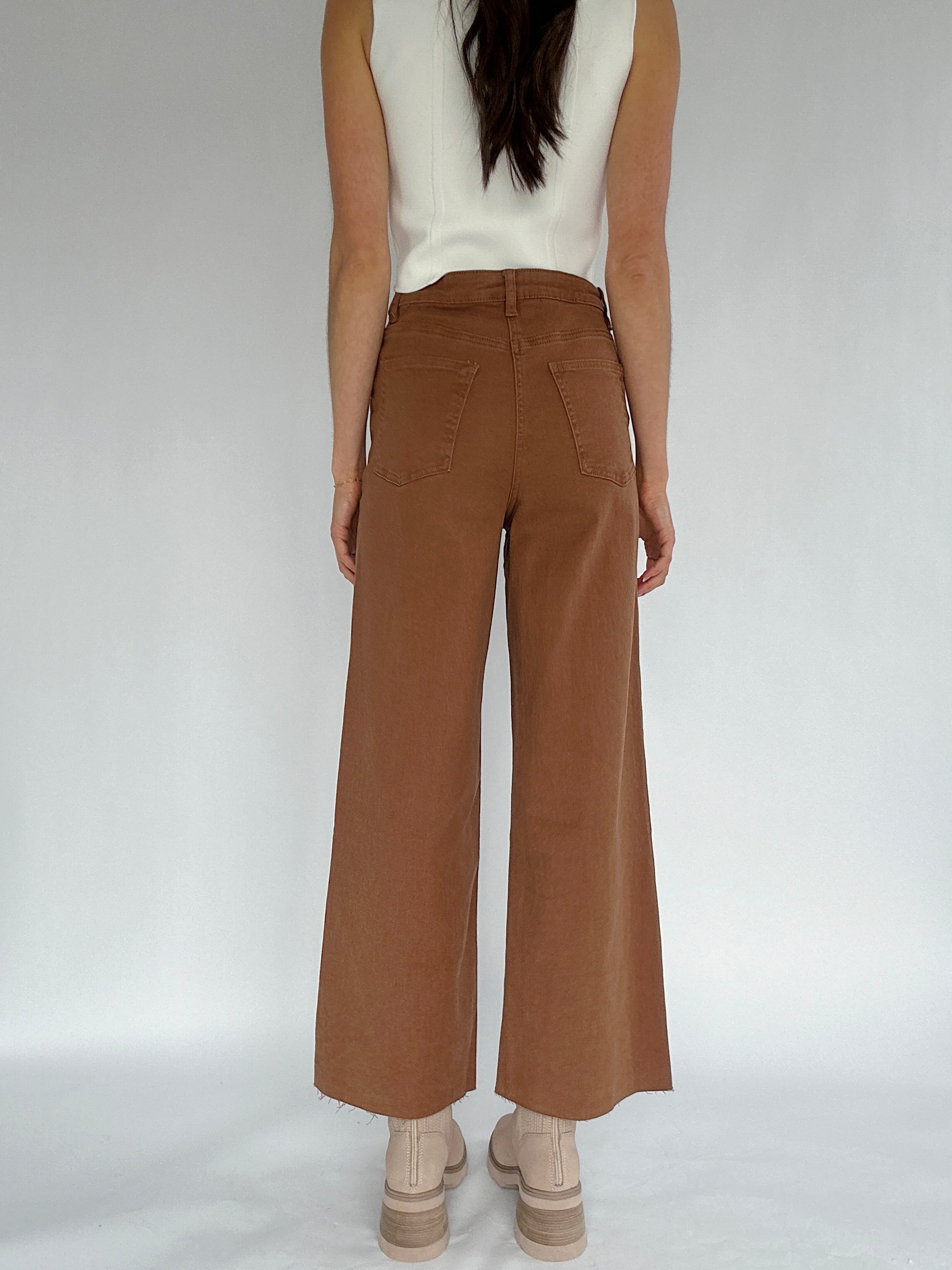 Person wearing brown wide-leg pants on a white background showing back
