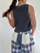 Person wearing a blue knitted sleeveless top and plaid pants with a white background to show solid back of top