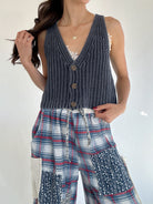 Woman wearing a navy knitted vest over plaid pants on a white background