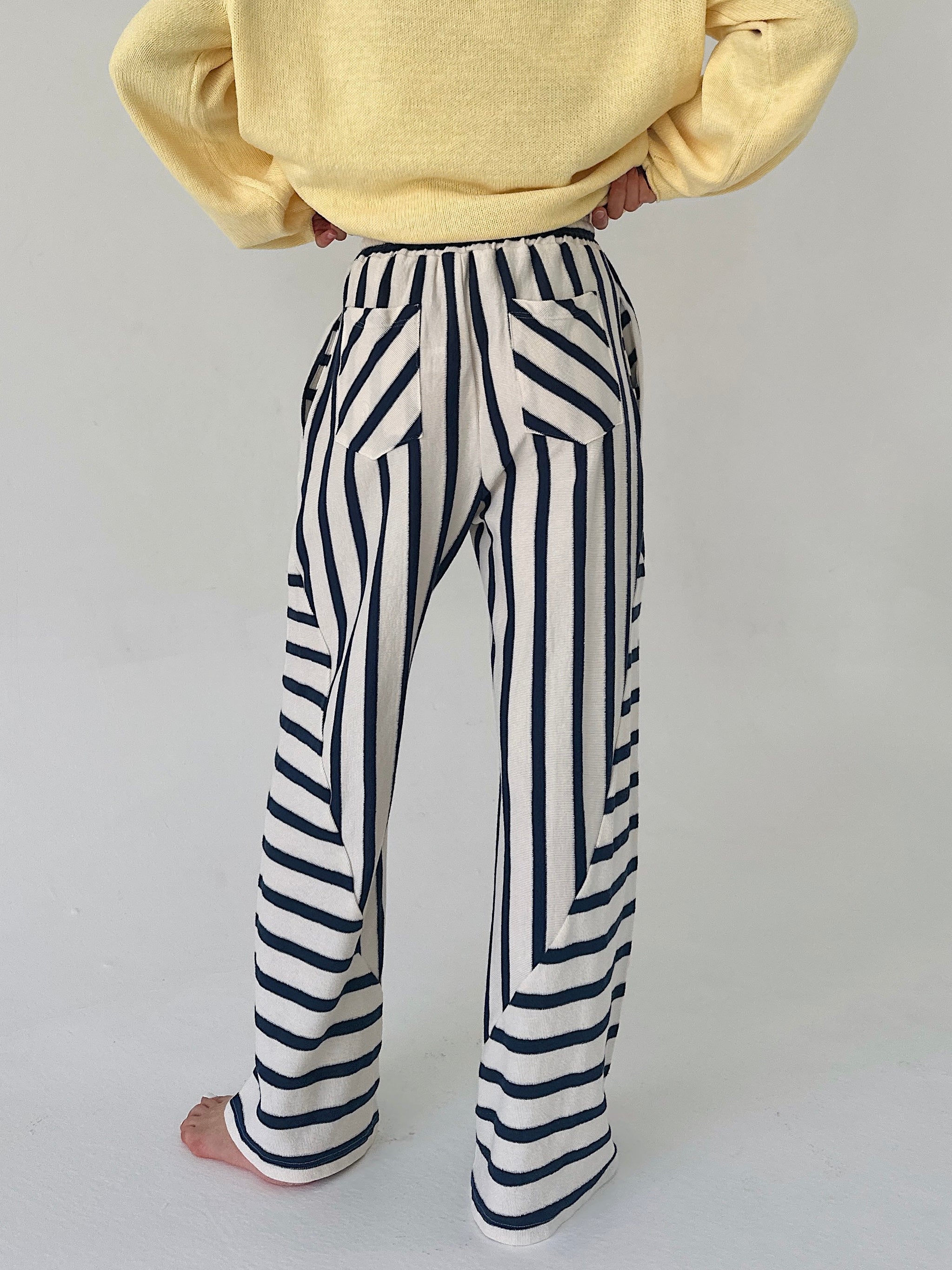 Person wearing a yellow sweater and black and white striped pants on a plain background showing back