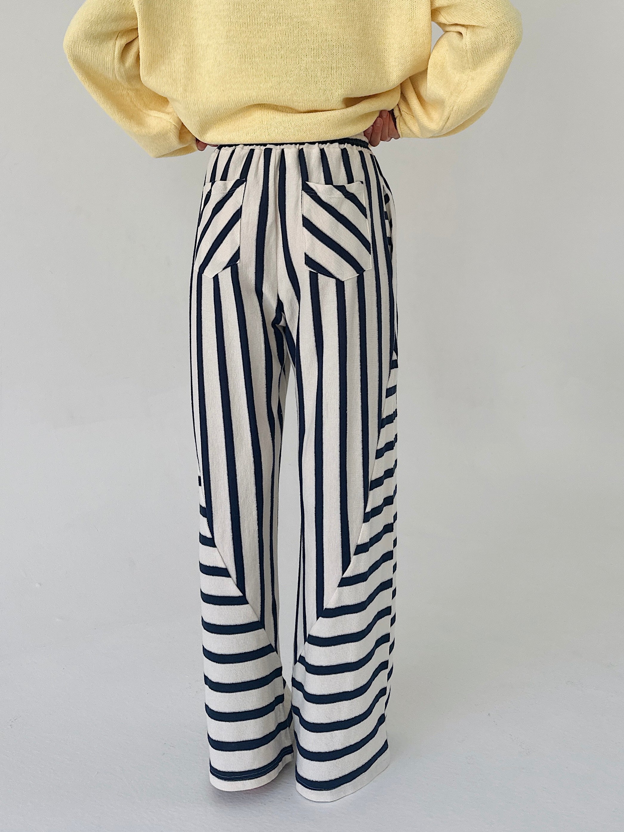 Person wearing a yellow sweater and black and white striped pants on a light gray background showing back