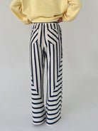 Person wearing a yellow sweater and black and white striped pants on a light gray background showing back