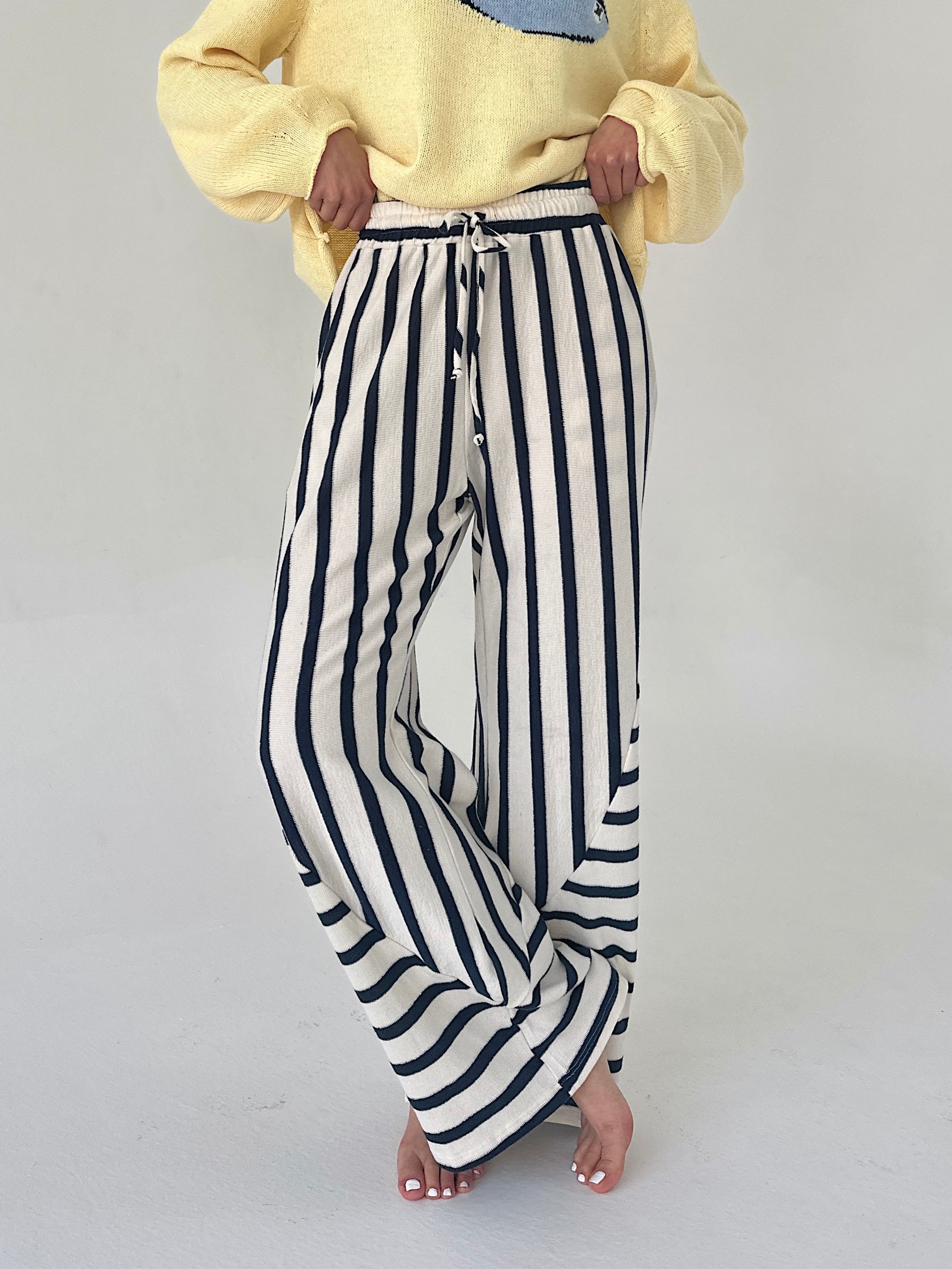 Person wearing a yellow sweater and black and white striped pants on a plain background